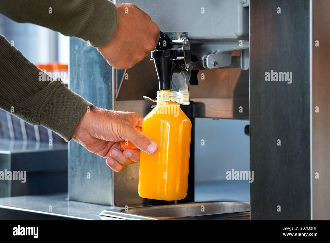 Man fills a plastic bottle with squeezed orange juice from a juicer in supermarket. Fresh orange juice in hypermarket. Stock Photo