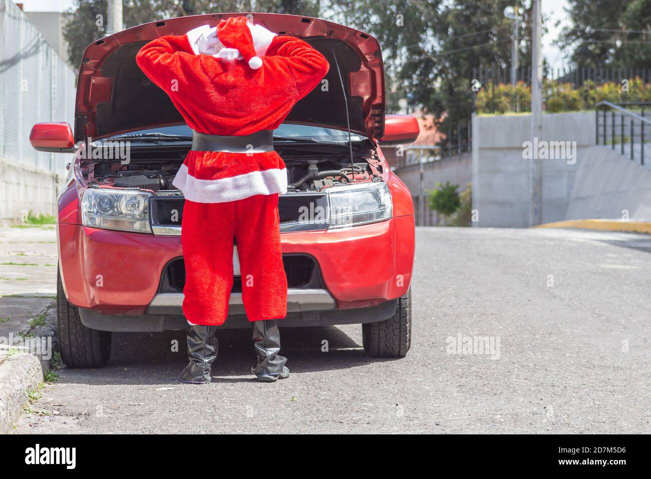 Santa Claus with his arms on his head in front of his car with the engine hood open worried that it is damaged at Christmas. Man disguised on the stre Stock Photo