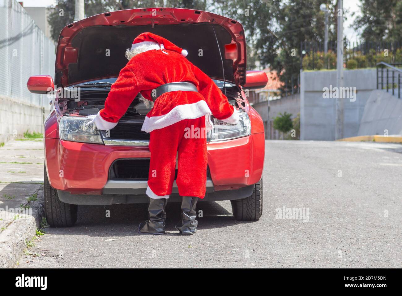 Santa Claus checking his car engine in front of his car that is damaged on Christmas. Man disguised on the street Stock Photo