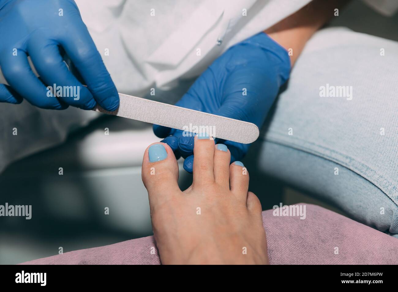 Pedicure in salon. Foot care treatment and nail. File filing with a nail file after applying gel polish. Master in blue gloves makes pedicure with man Stock Photo