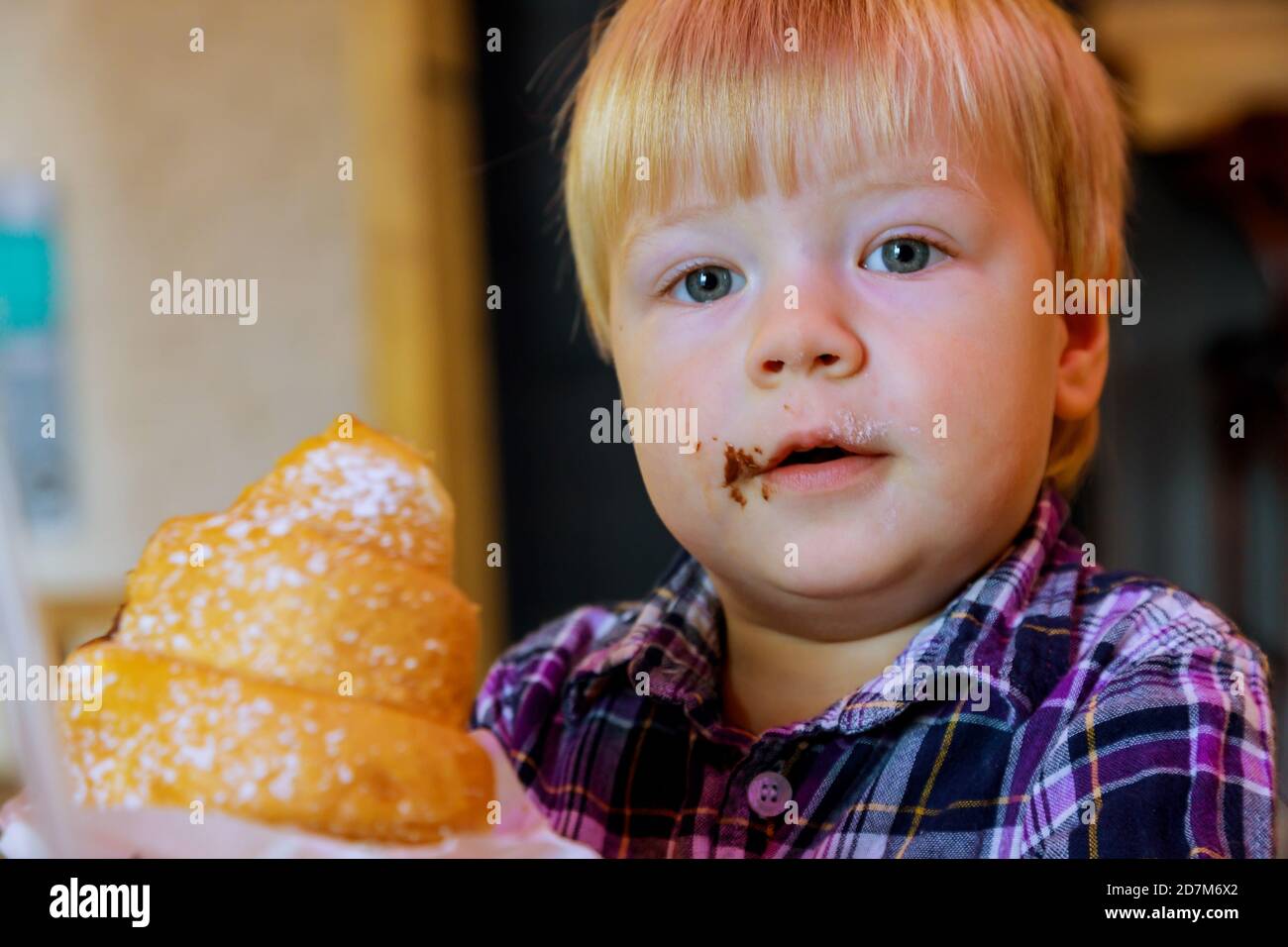 Breakfast time beautiful baby happy boy eating croissant in coffee shop. Stock Photo