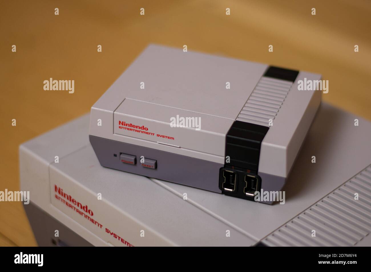 A Nintendo Entertainment System Classic Edition on Top of an Original Nintendo Entertainment System, on a wood floor. Comparison of the original NES a Stock Photo