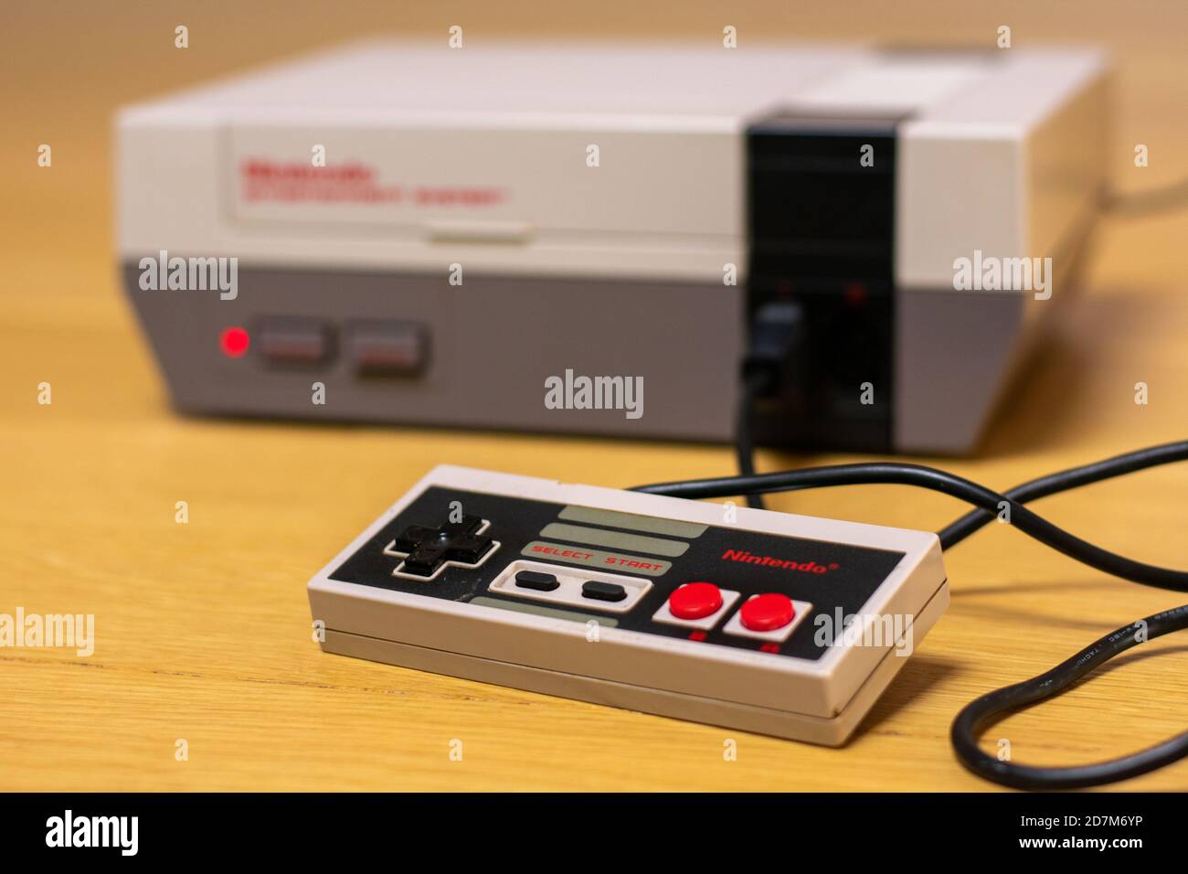 The Controller of a Nintendo Entertainment System on a wooden floor plugged into the console. Stock Photo