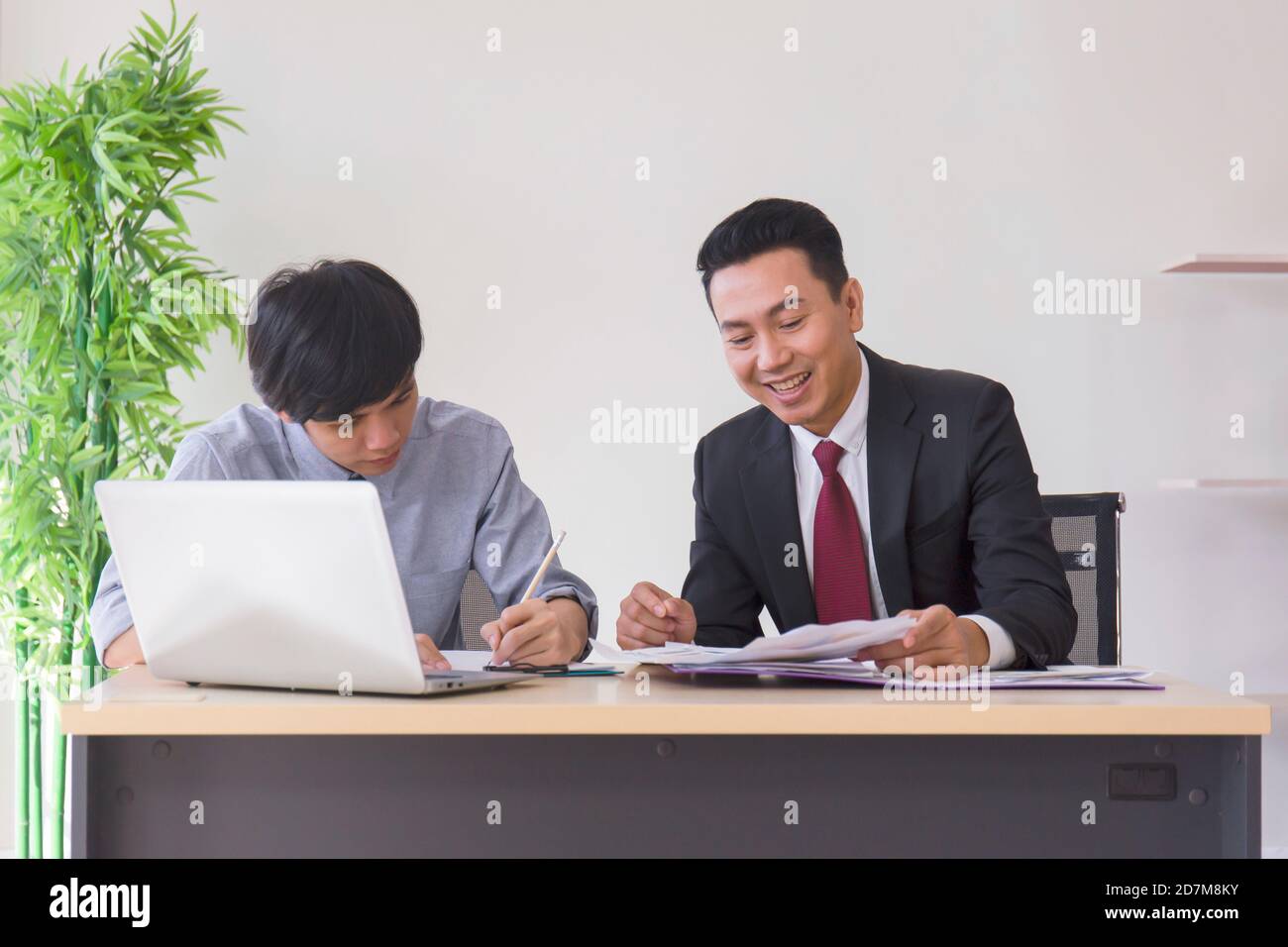 An Asian male supervisor teaches the newcomer to the office on his desk. Stock Photo