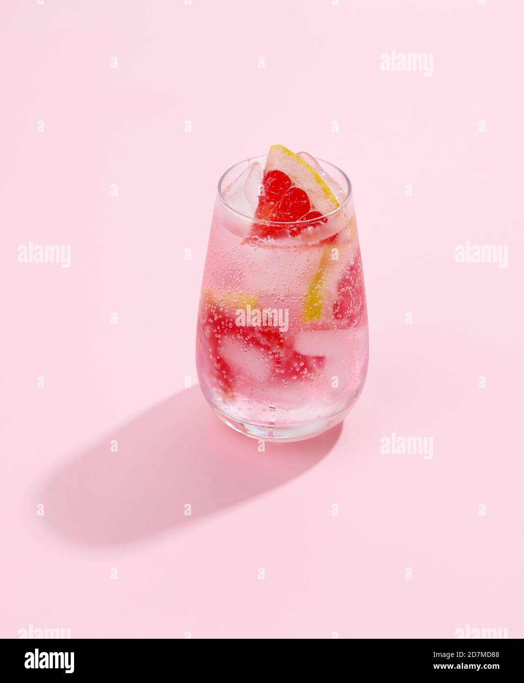 glass of grapefruit soft drink with long shadow on pink background