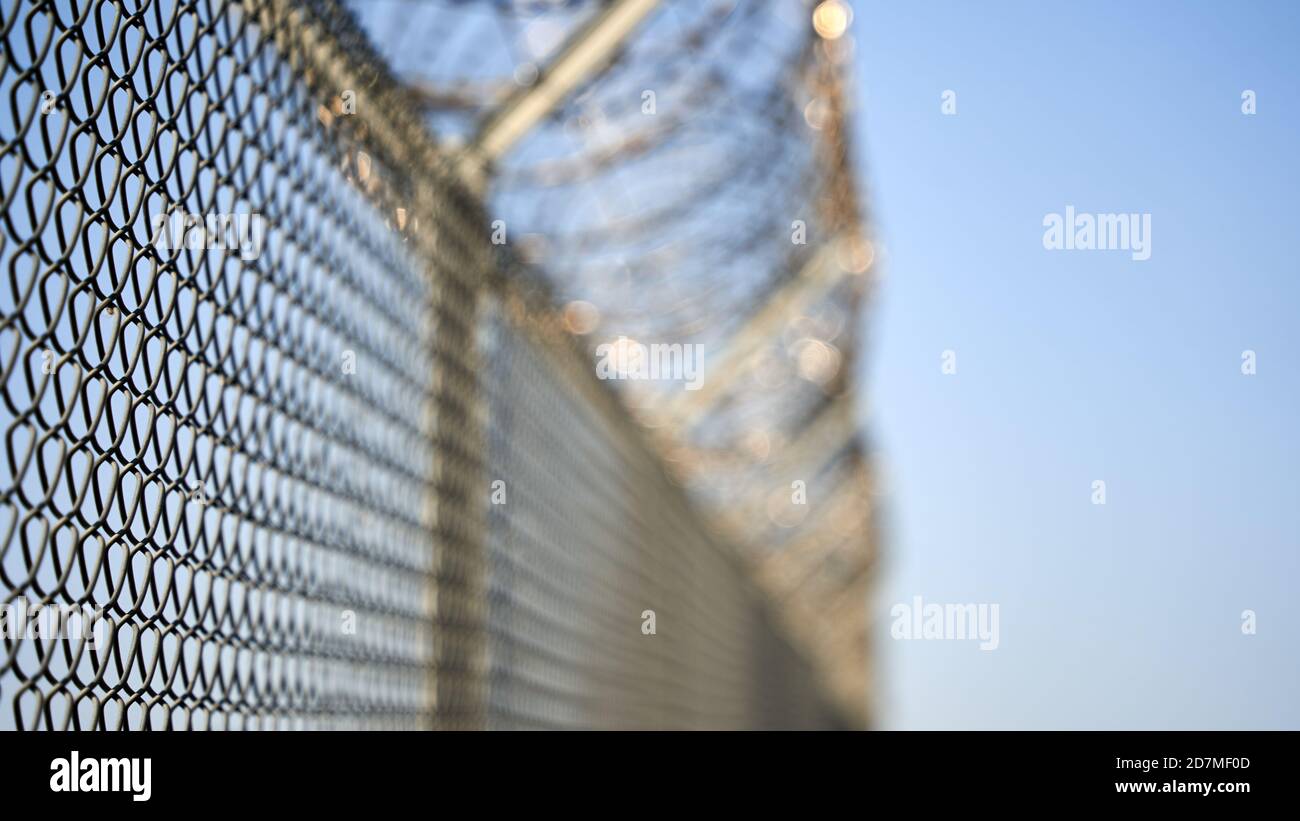 Chain-link fence with overlying barbed wire fence against a blue background. Copy-space. selective focus. Germany. Stock Photo