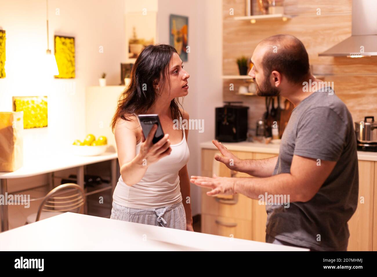 Wife fighting with cheating husband holding phone with texts from another woman. Heated angry frustrated offended irritated accusing her man of infidelity showing him messages. Stock Photo