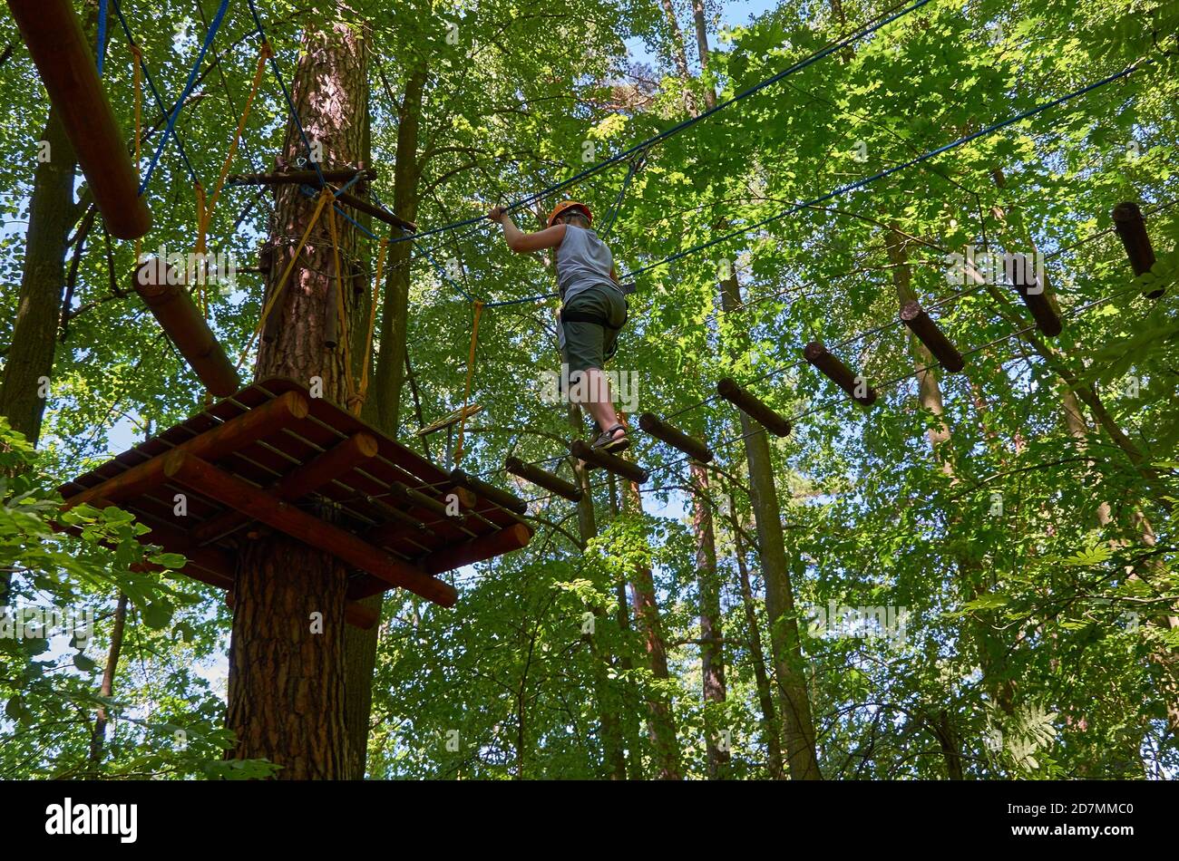 A boy with a helmet and insurance passes a high-altitude obstacle course. Workout Stock Photo