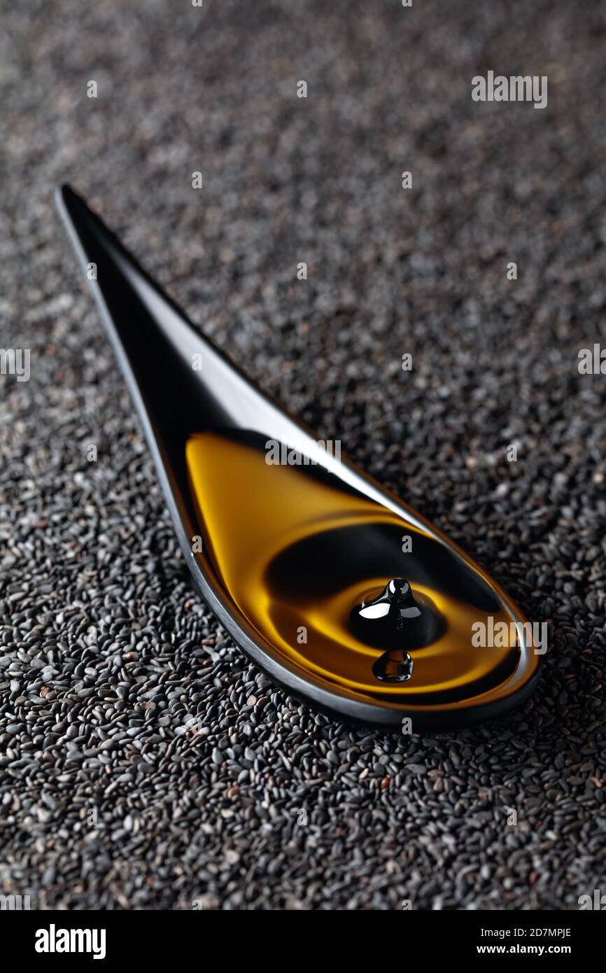 Sesame oil and raw black sesame seeds. A drop of oil fall in a small