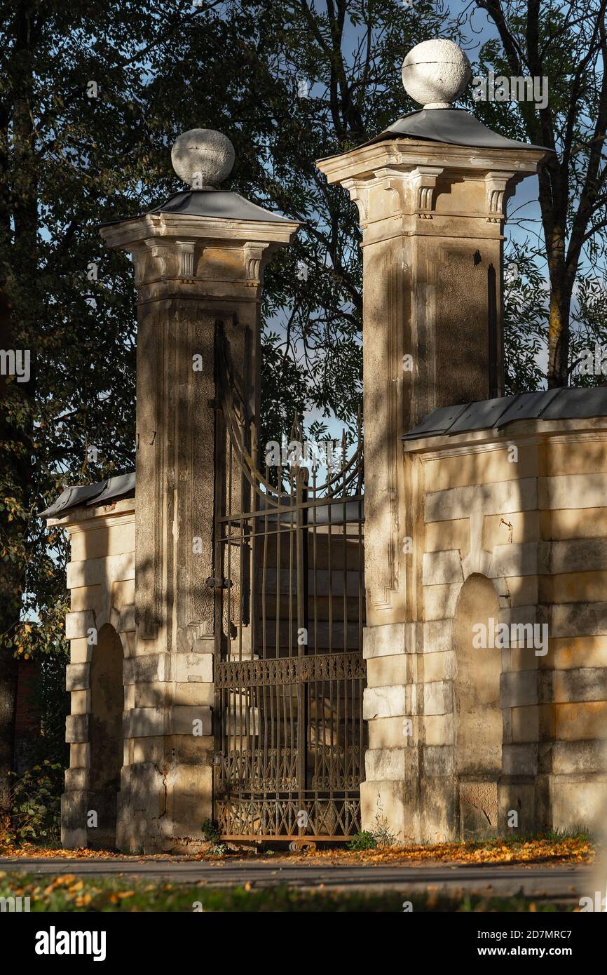 The ancient ornate neoclassical entrance gate of Tyshkevich manor in the park alley is lit by the evening sun in the autumn in Traku Voke, Lithuania Stock Photo