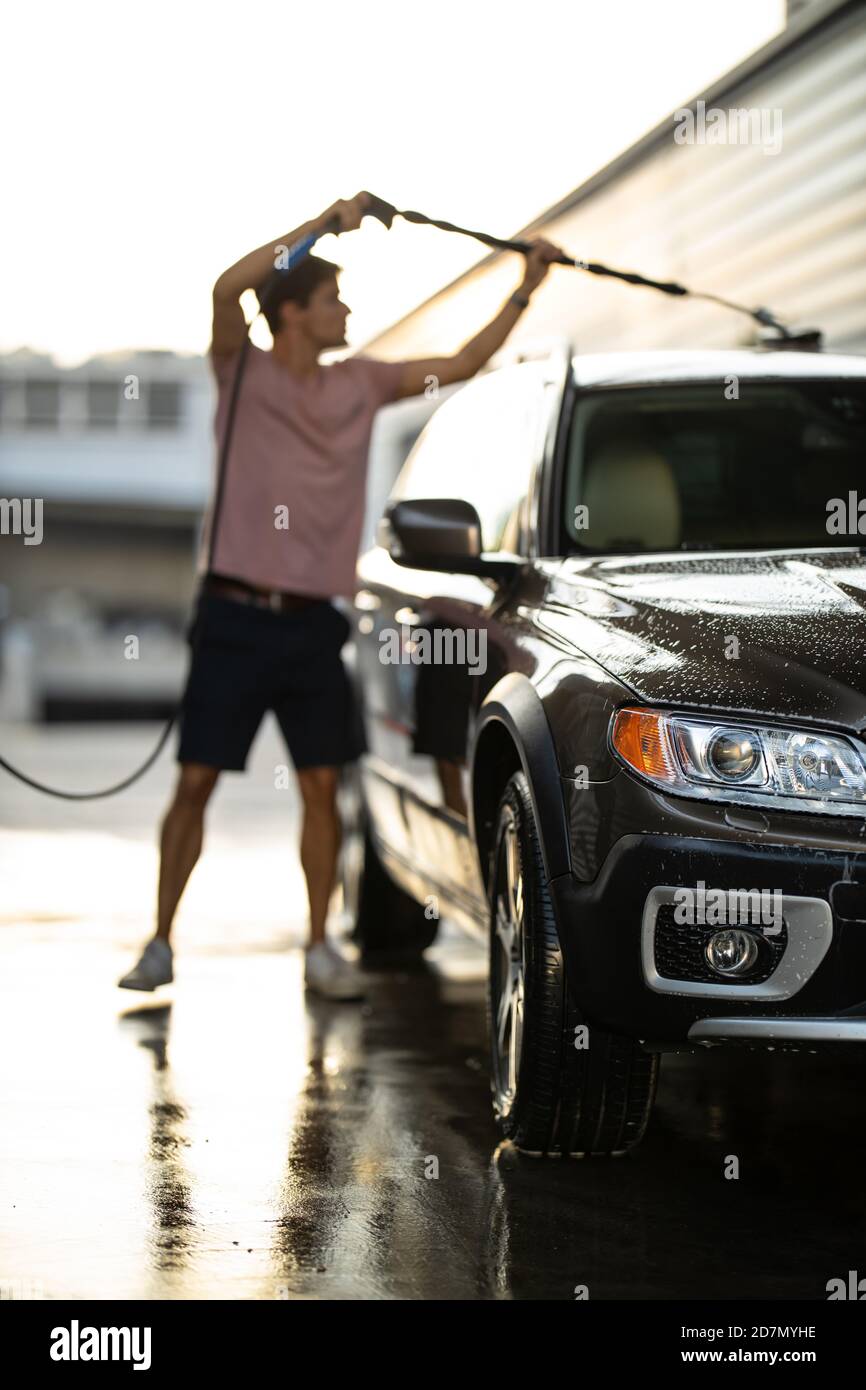 Young man washing his beloved car carefully in a manual car wash to