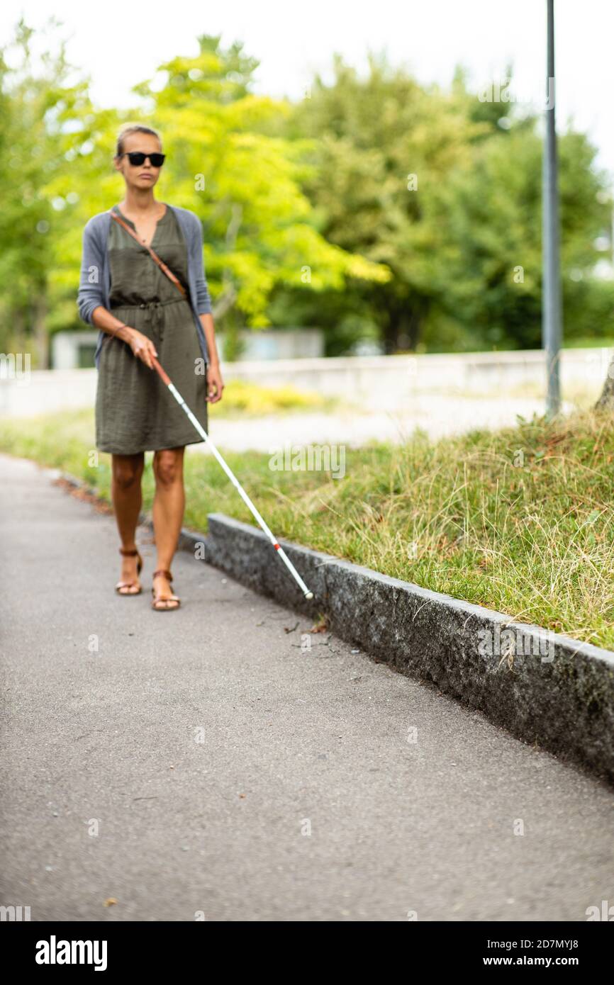 Blind woman walking on city streets, using her white cane to