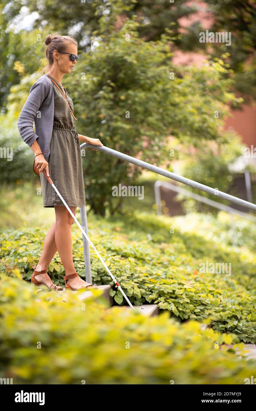 Blind woman walking on city streets, using her white cane to