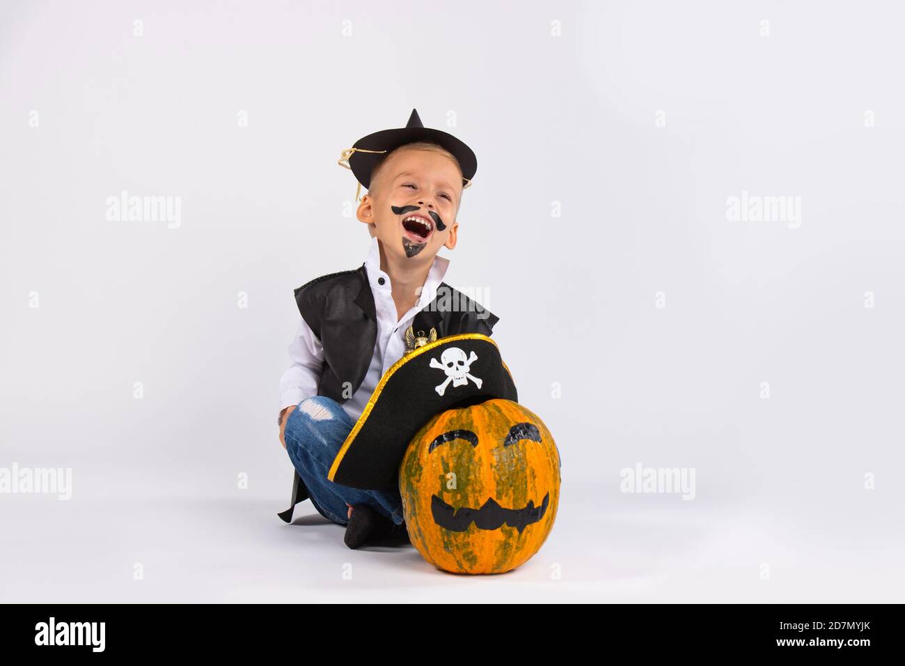 Boy in black handmade hat . Nearby is pumpkin in pirate hat. Both are