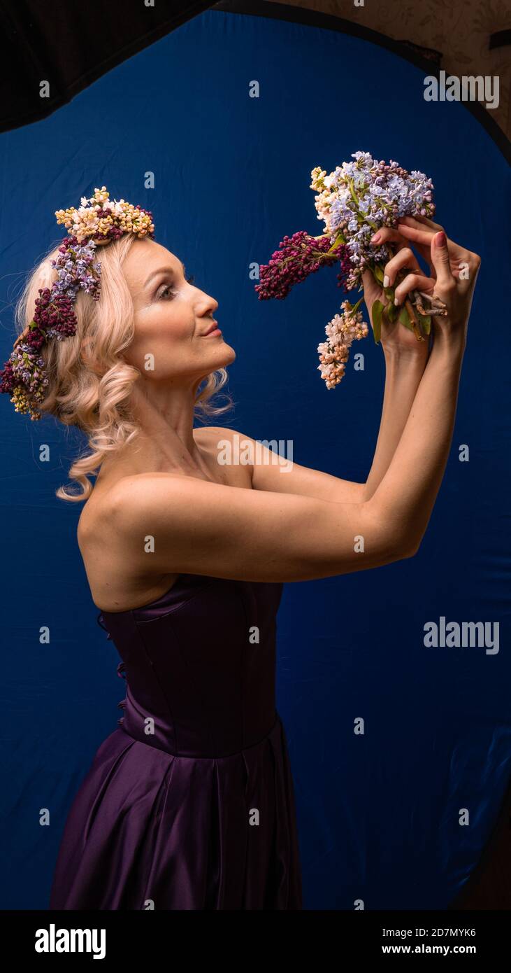 Happy young lovely in a lilac wreath with a lovely smile has fun on a blue background, with bright daylight Stock Photo