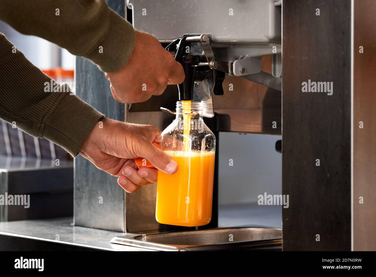 Man fills a plastic bottle with fresh orange juice in supermarket. Fresh orange juice in hypermarket.  Stock Photo