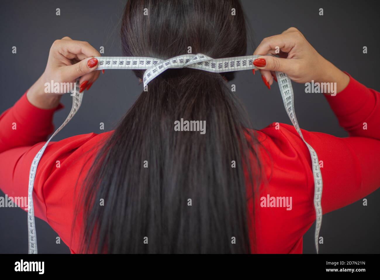 Female fashion designer in red dress wrapped her hair with tape measure Stock Photo