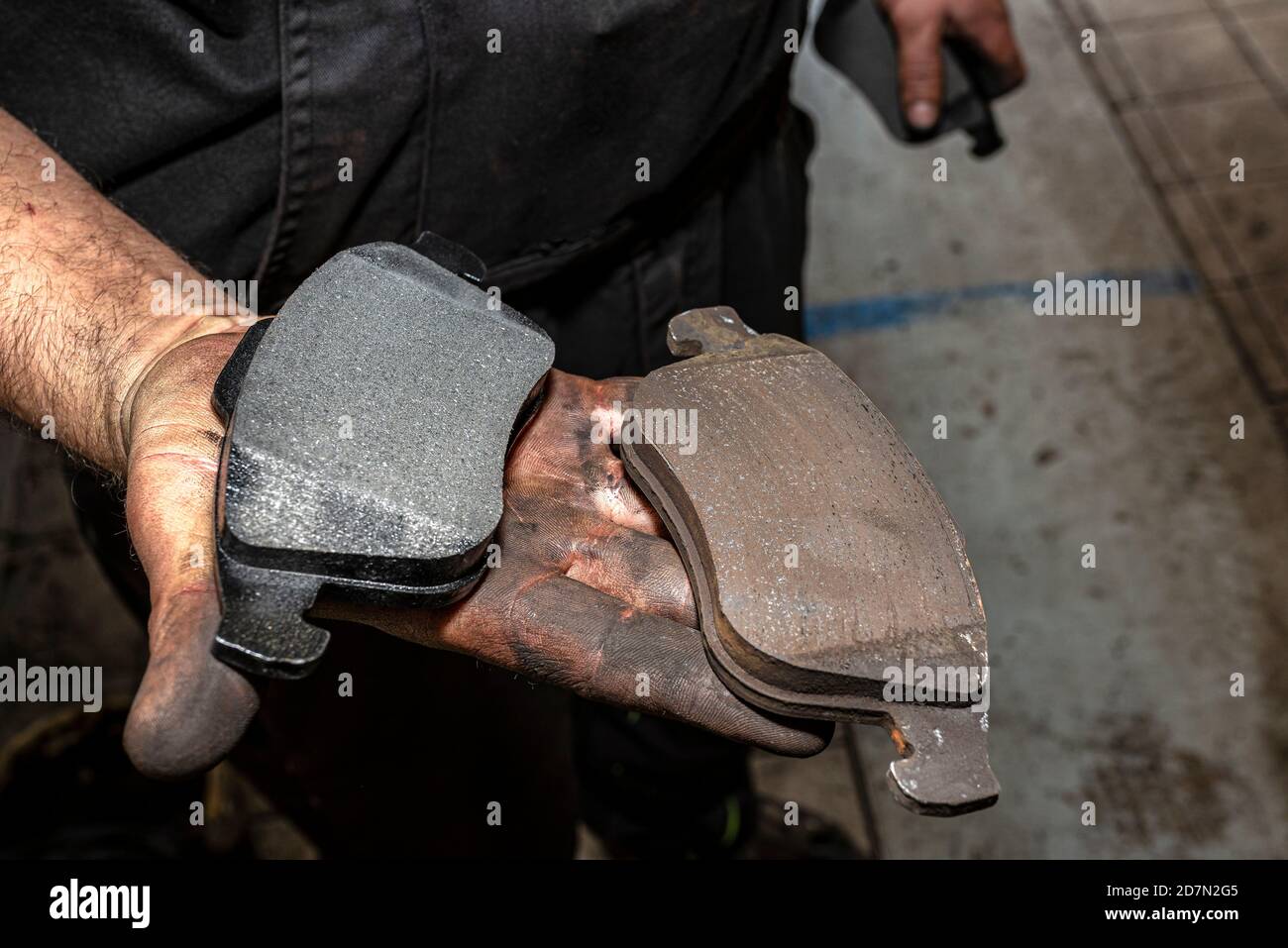 A car mechanic holds in a dirty, open hand a new and old brake pad