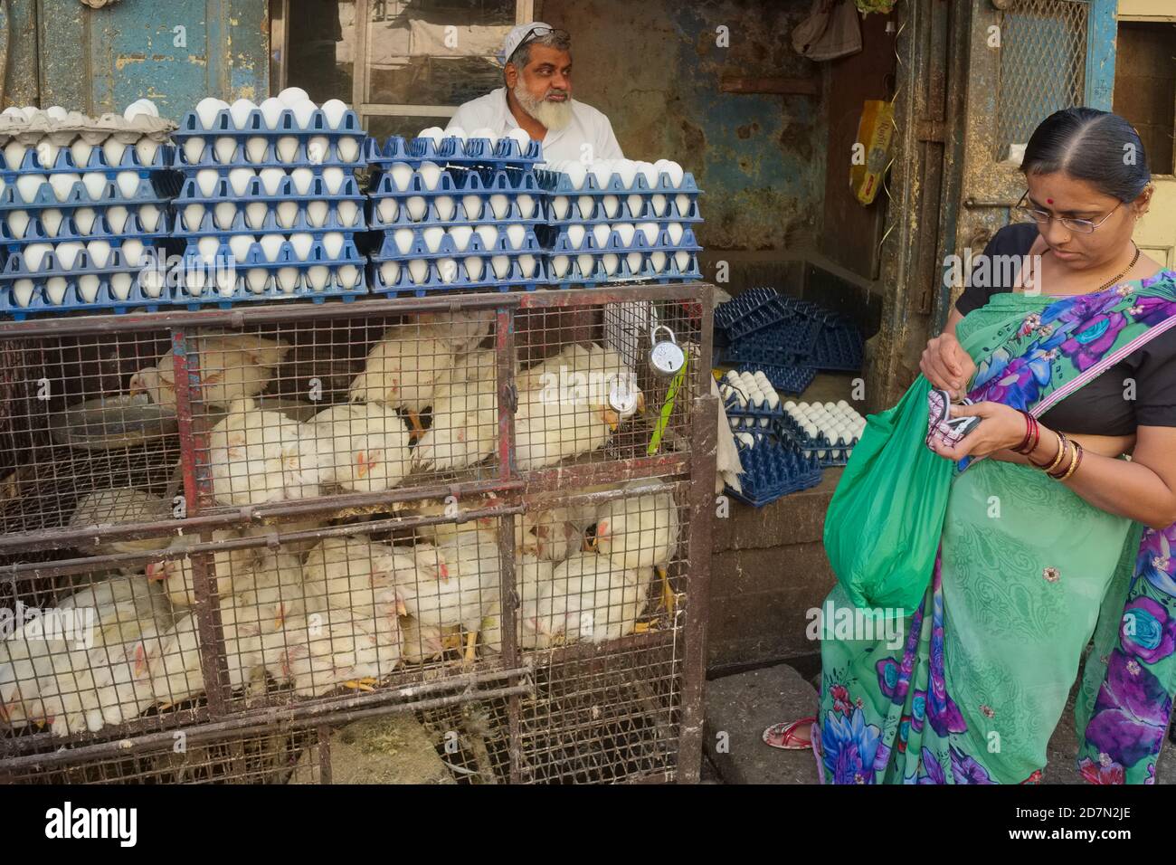 At a chicken and egg shop in Byculla, Mumbai, India, Hindu a housewife gingerly pulls money from her purse to pay the Muslim vendor Stock Photo
