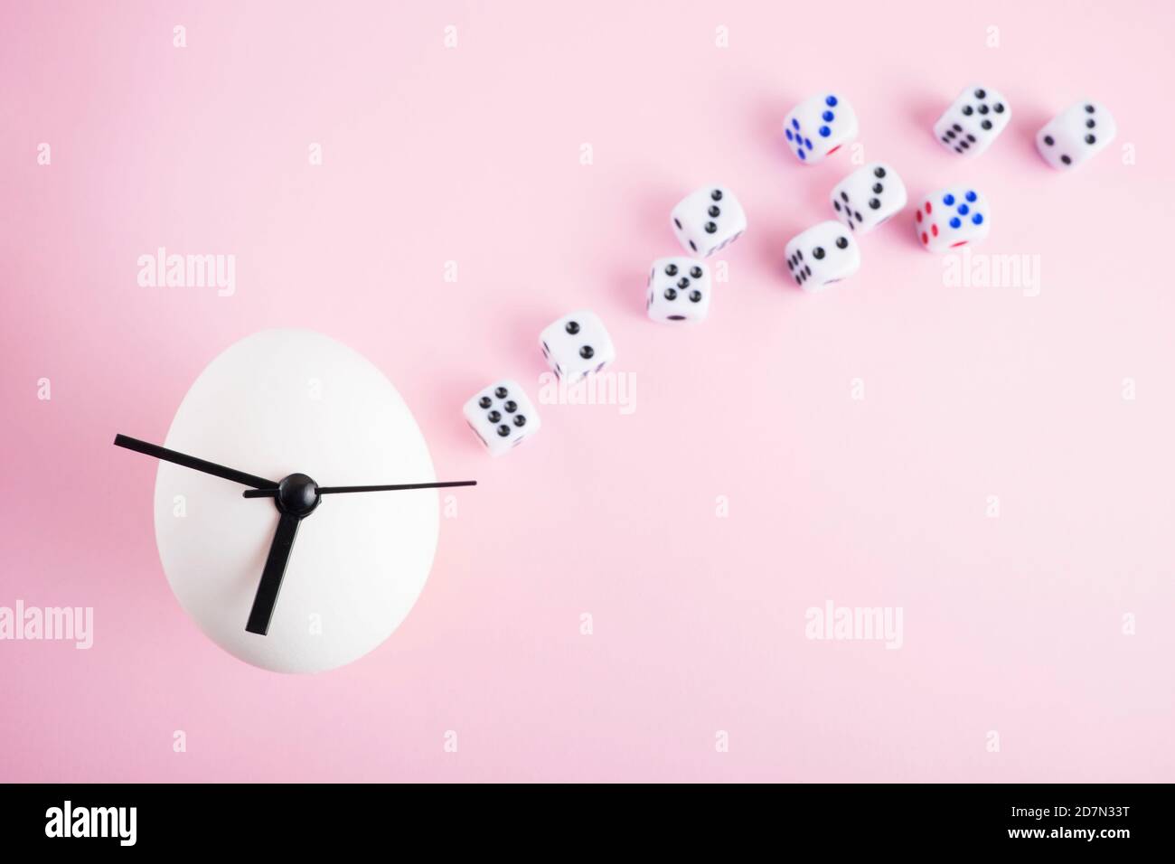 Egg clock and dice on pink background. Stock Photo