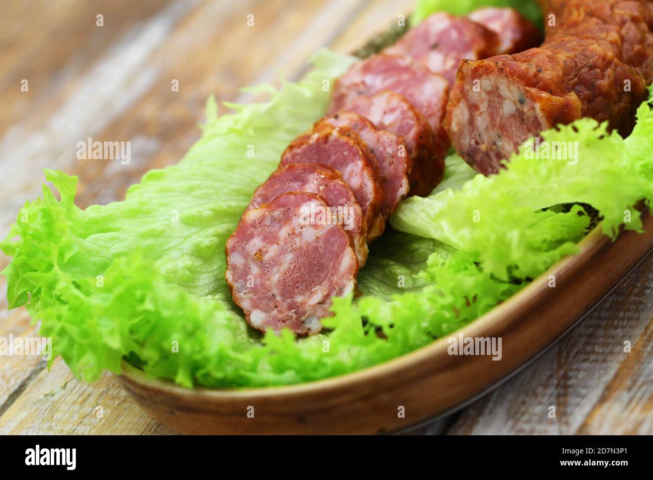 Slices of smoked pork sausage on lettuce leaves, closeup Stock Photo