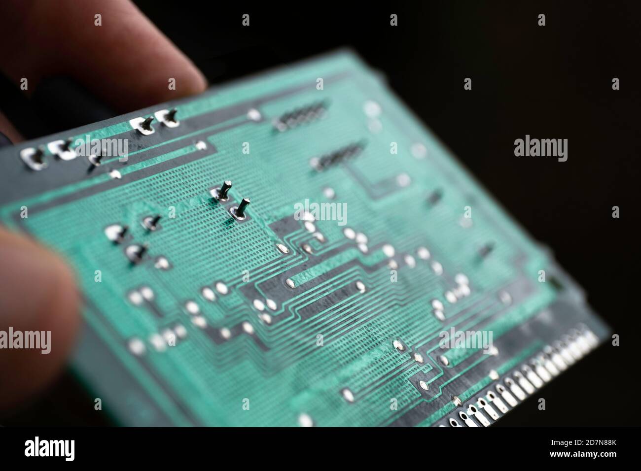 Fingers hold a green electronic circuit board with many electrical components against a black background Stock Photo