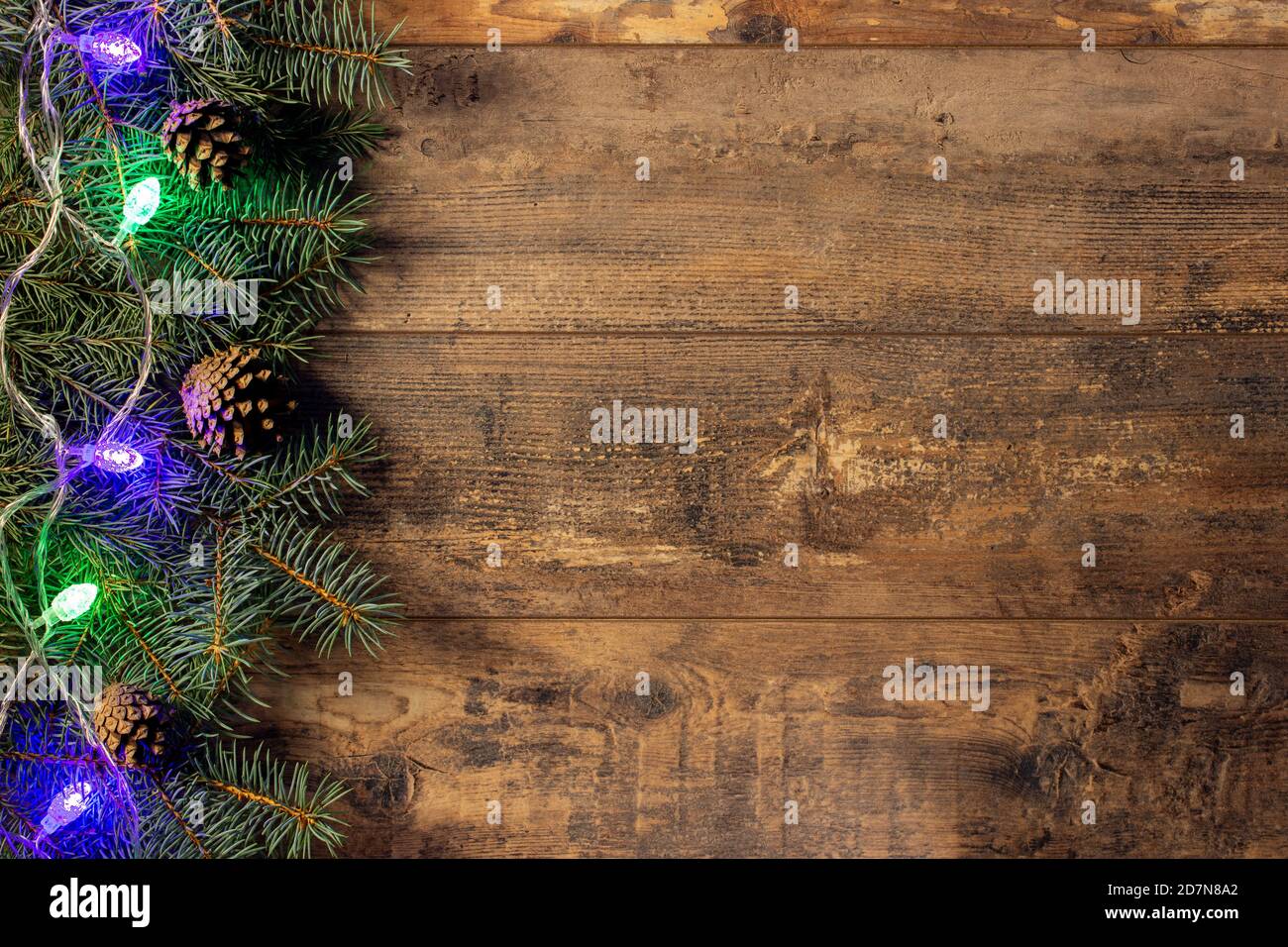 green fir branches and Christmas lights on dark wooden table background ...