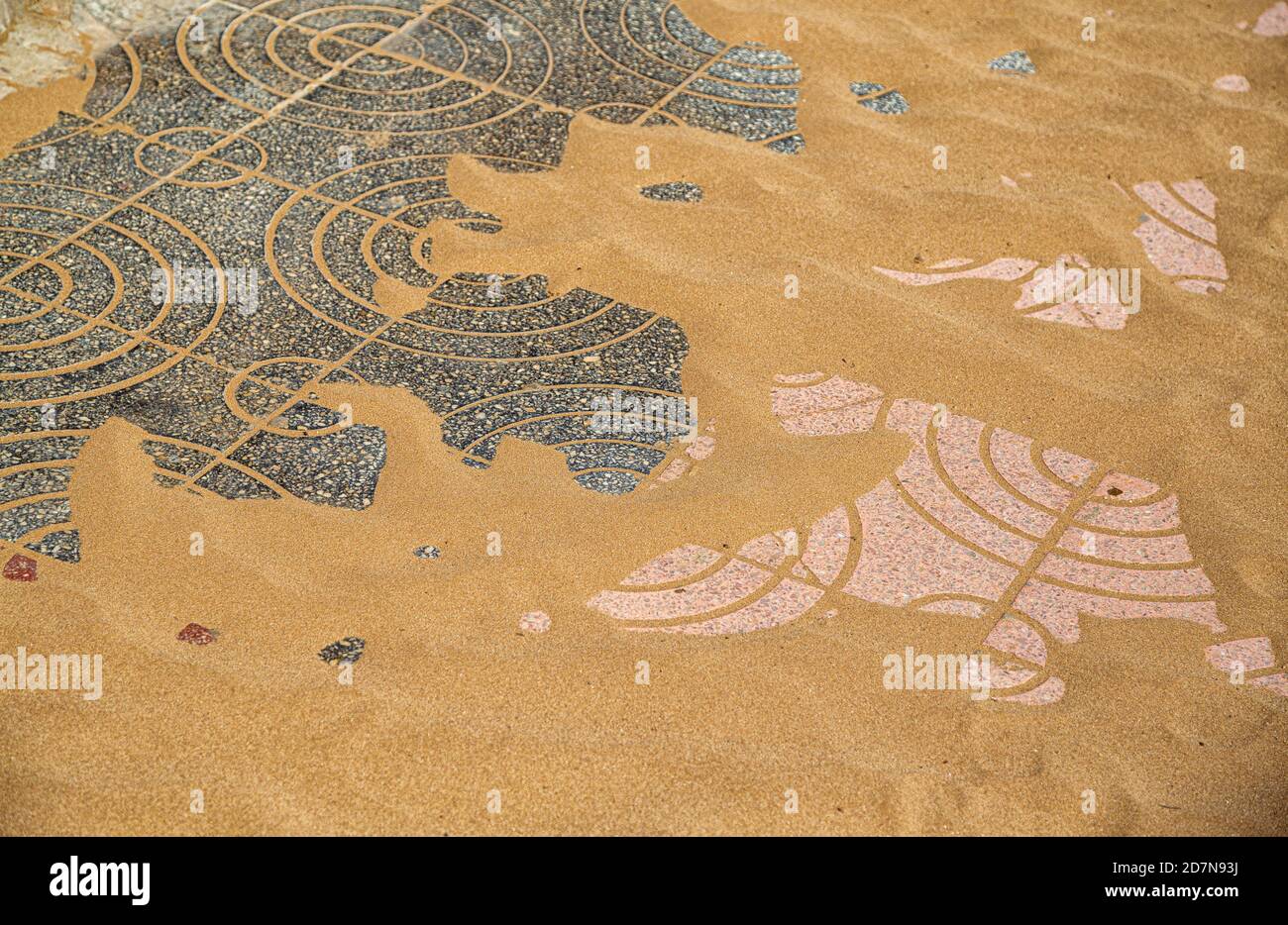 Paving stone with a geometric design emerging from under the sand Stock Photo