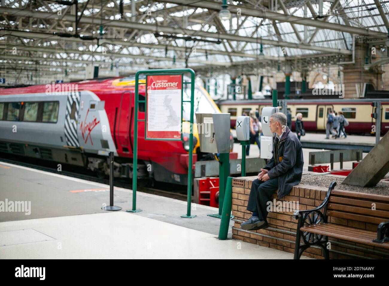 Glasgow Central Station July 2010. A man sits on a wall after passengers have boarded the train, appearing to think or ponder. Virgin trains. Street. Stock Photo