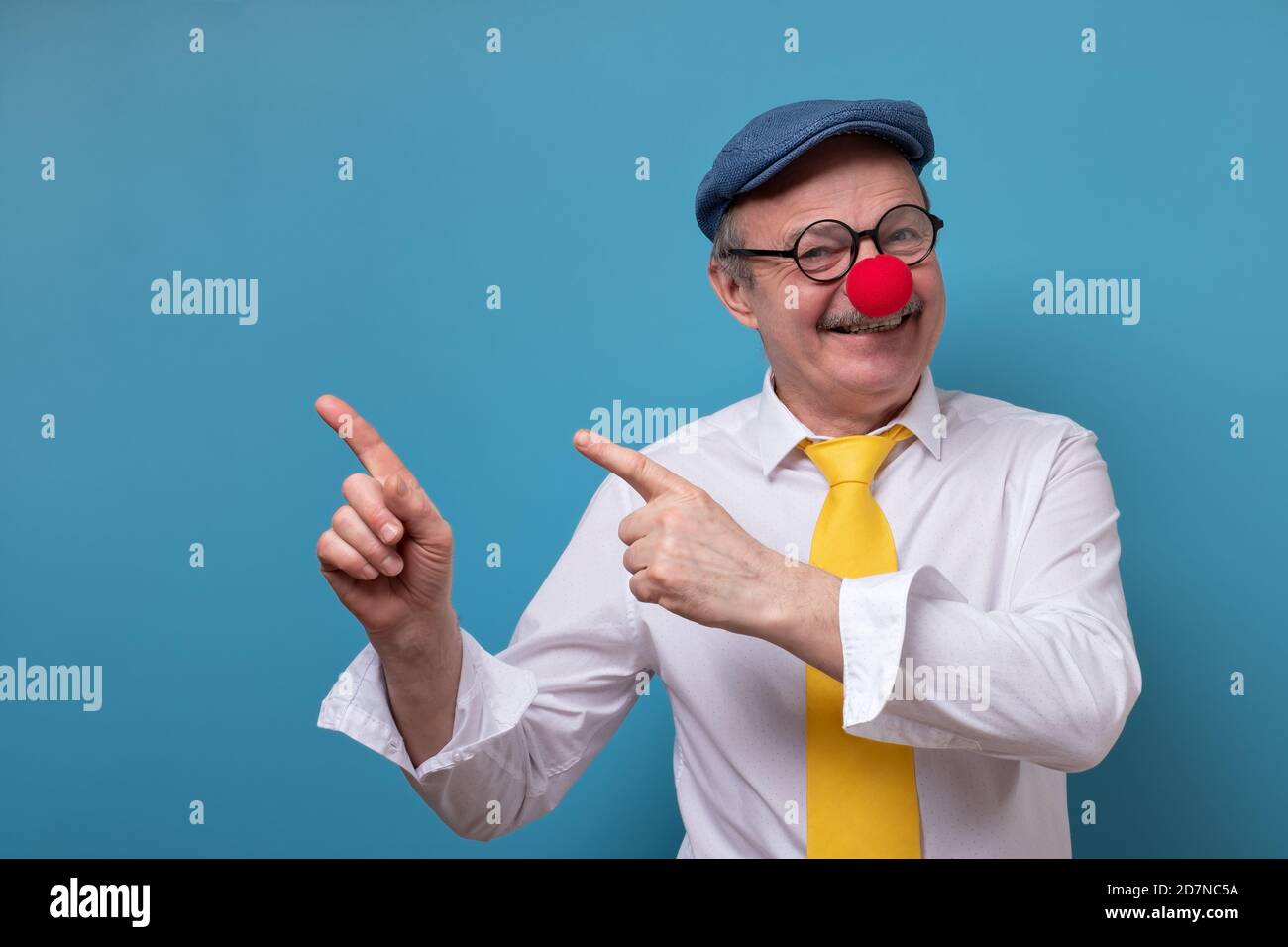 Senior cheerful man with red nose pointing with index finger aside. Stock Photo