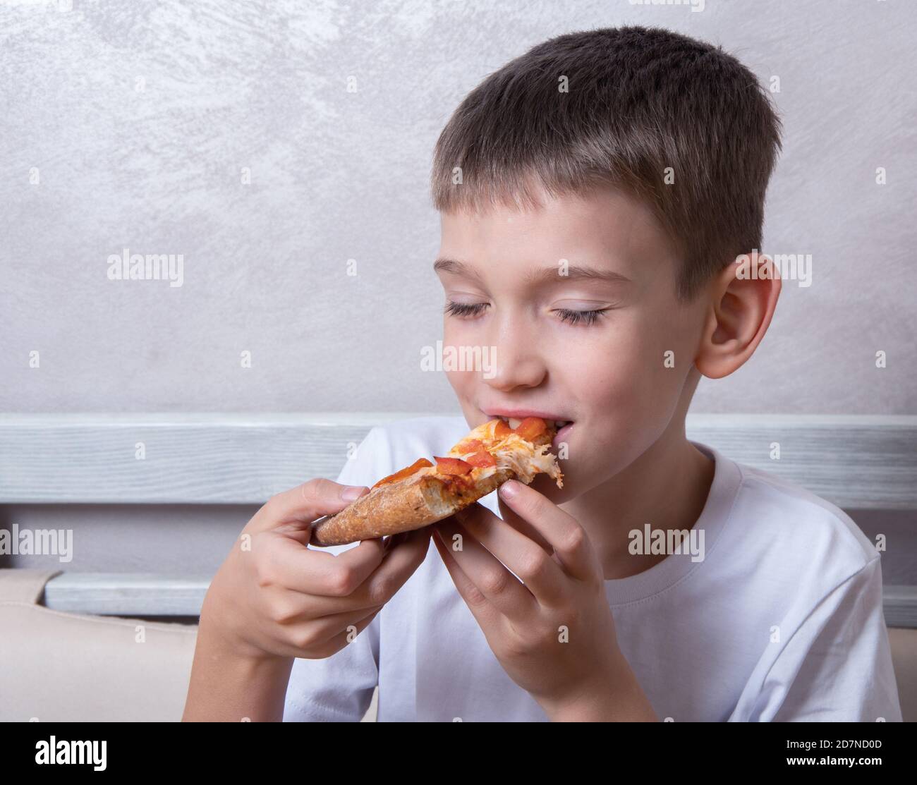 Cute boy eating a slice of pepperoni and cheese pizza, the child closed