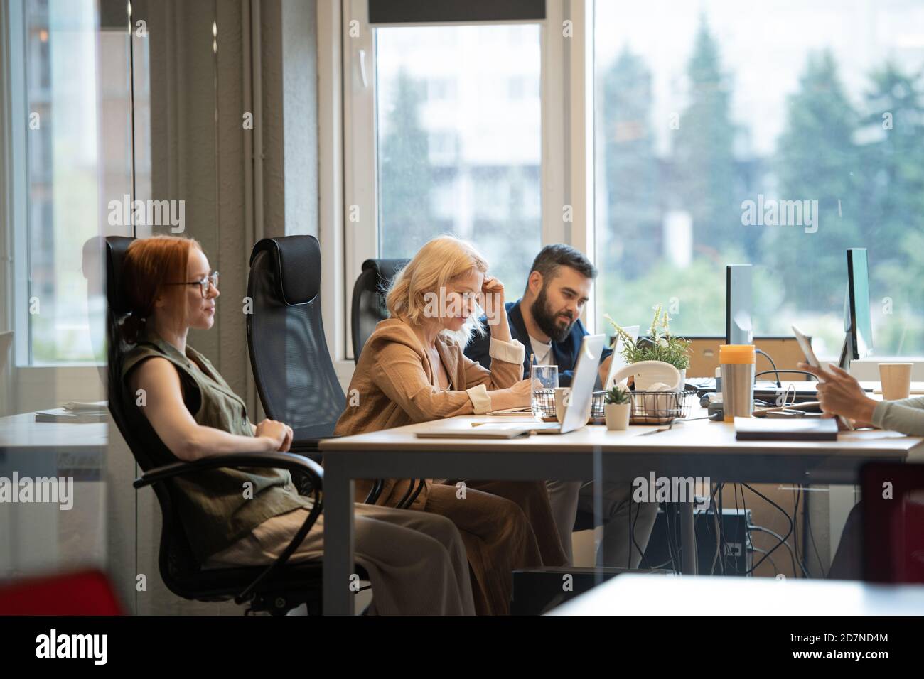 Happy mature businesswoman making notes by desk between two young colleagues Stock Photo