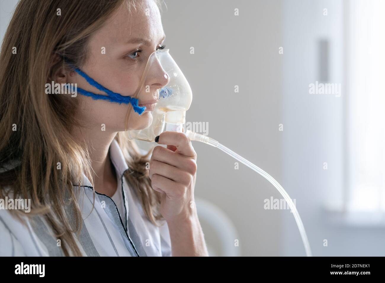 Sick young female patient holding oxygen mask by her mouth and nose Stock Photo