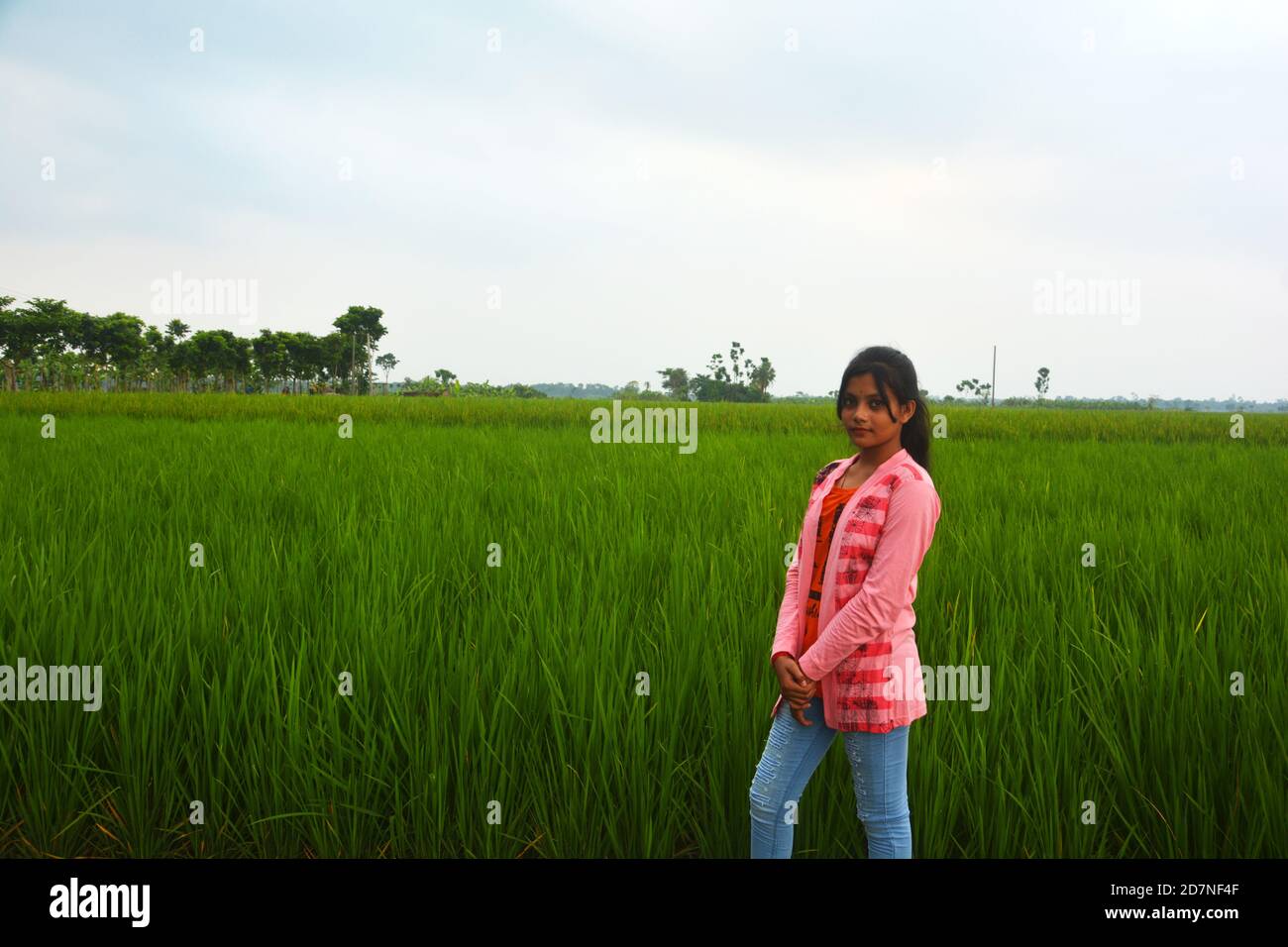 A teenage girl wearing jeans, pink uppers and white shoes standing in a paddy field, selective focusing Stock Photo