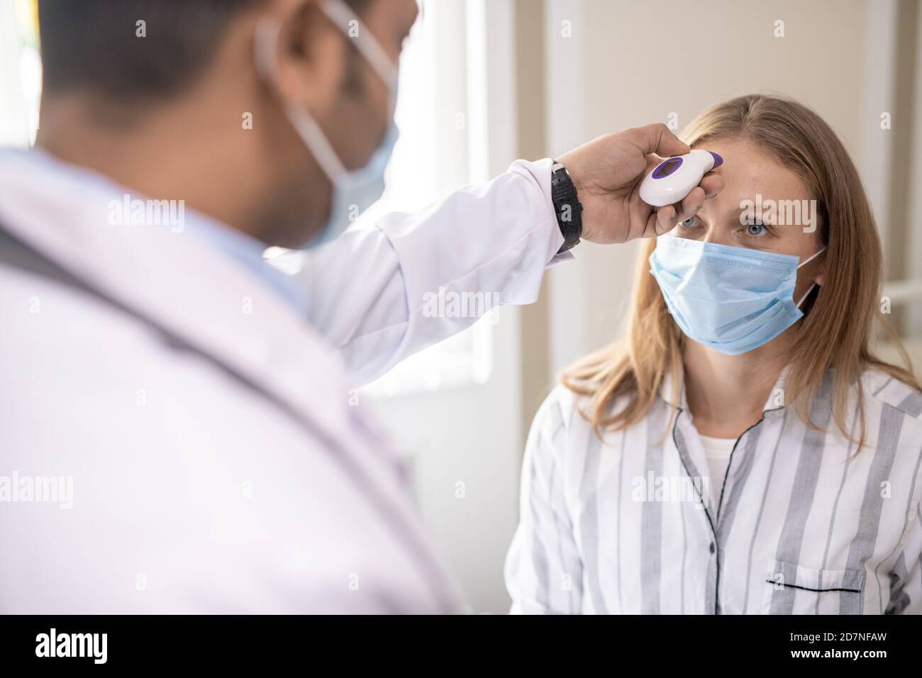 Young female patient in protective mask having her body temperature measured Stock Photo
