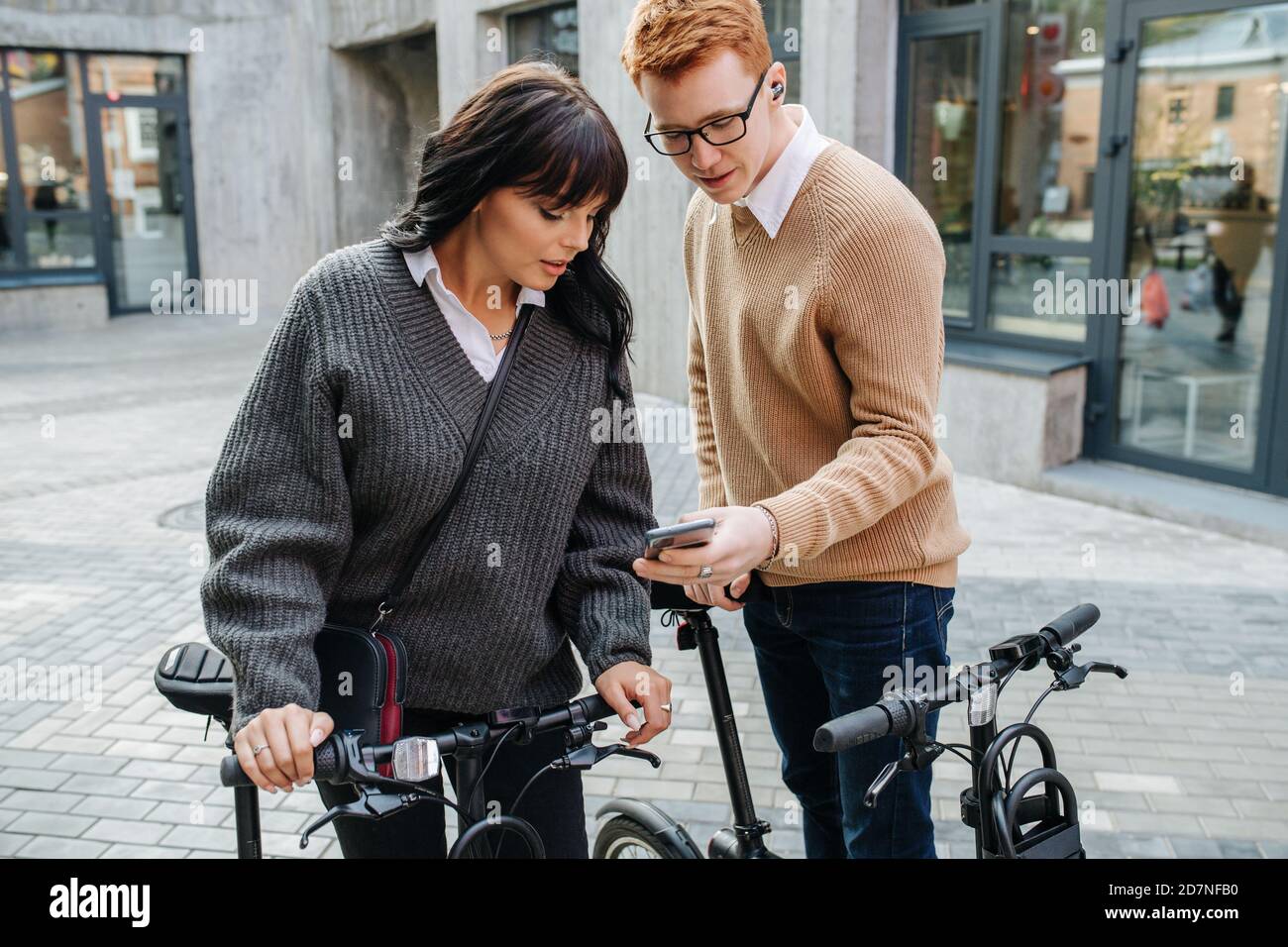 Lost young couple tugging ebikes, looking at phone screen, figuring the way Stock Photo