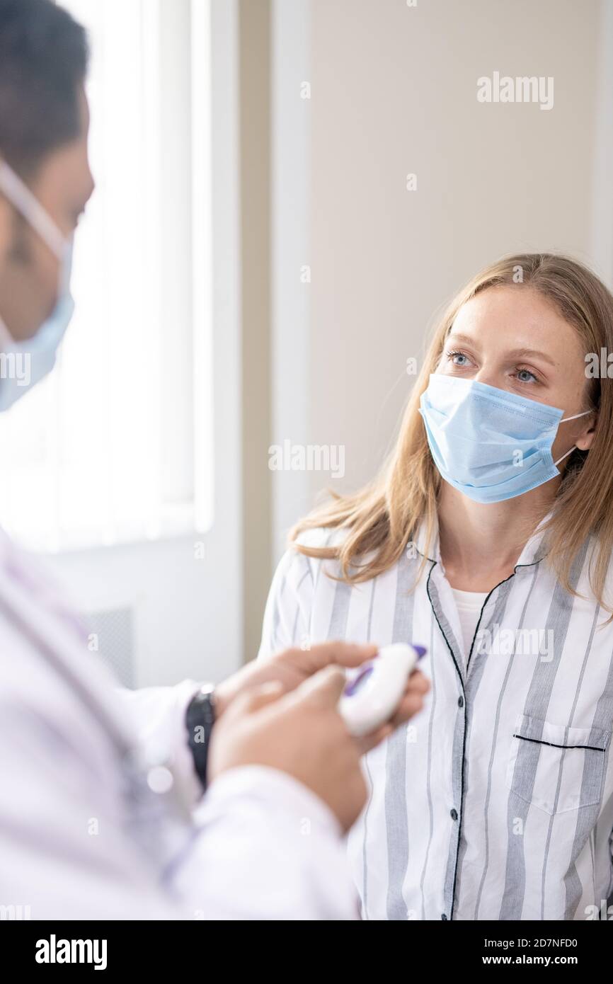 Young female patient in mask looking at her doctor during medical consultation Stock Photo