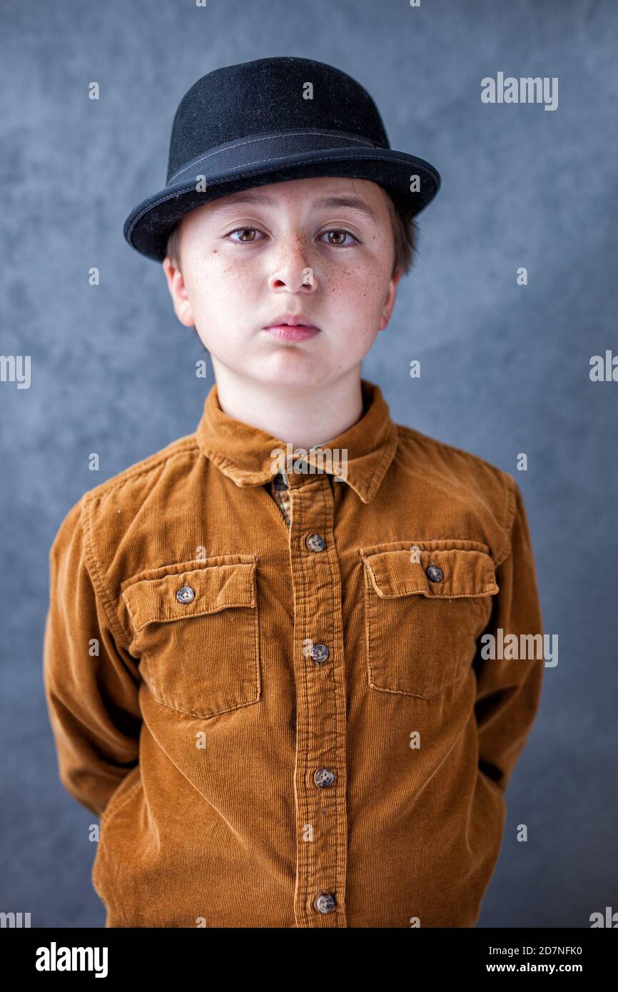 Handsome multi-racial Asian Caucasian little juvenile delinquent boy wearing gold rust colored corduroy button up shirt and black pork pie fedora hat Stock Photo