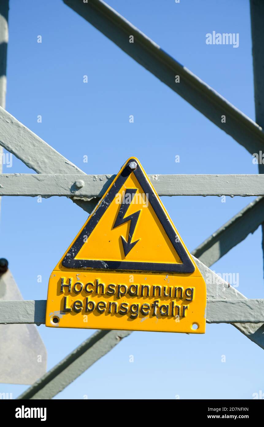 High voltage overhead electrical power line and yellow flash danger sign in a rural landscape in the countryside in Germany, Western Europe Stock Photo