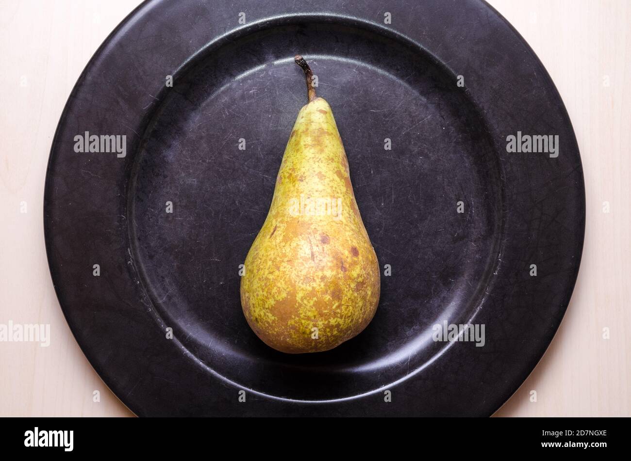 One single pear fruit, Pyrus, flat lay on dark black round plate on wooden table or desk, food photography, close-up, copy space Stock Photo