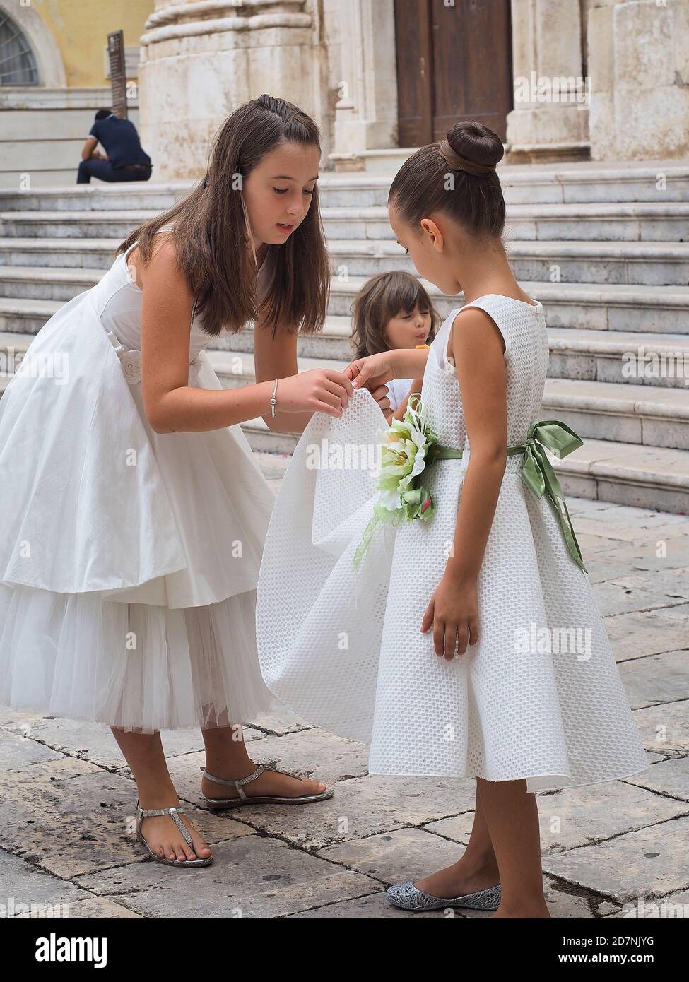 MONOPOLI, ITALY - 09/09/2917: Thre little caucasian bridesmaids in white dress in front of church. Summer day. Stock Photo