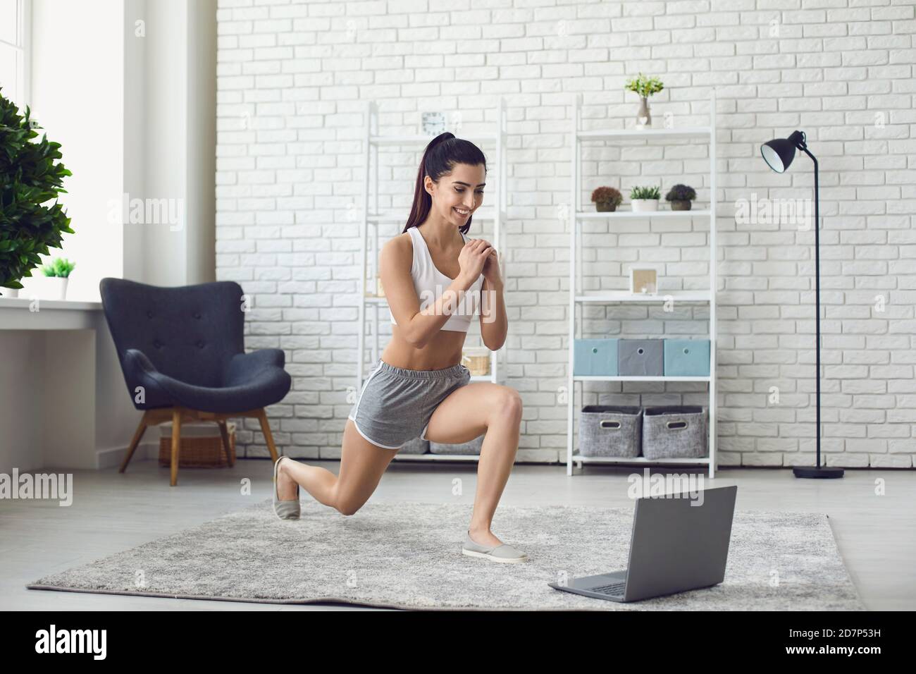Smiling girl doing sports workout during online lesson on laptop at home Stock Photo