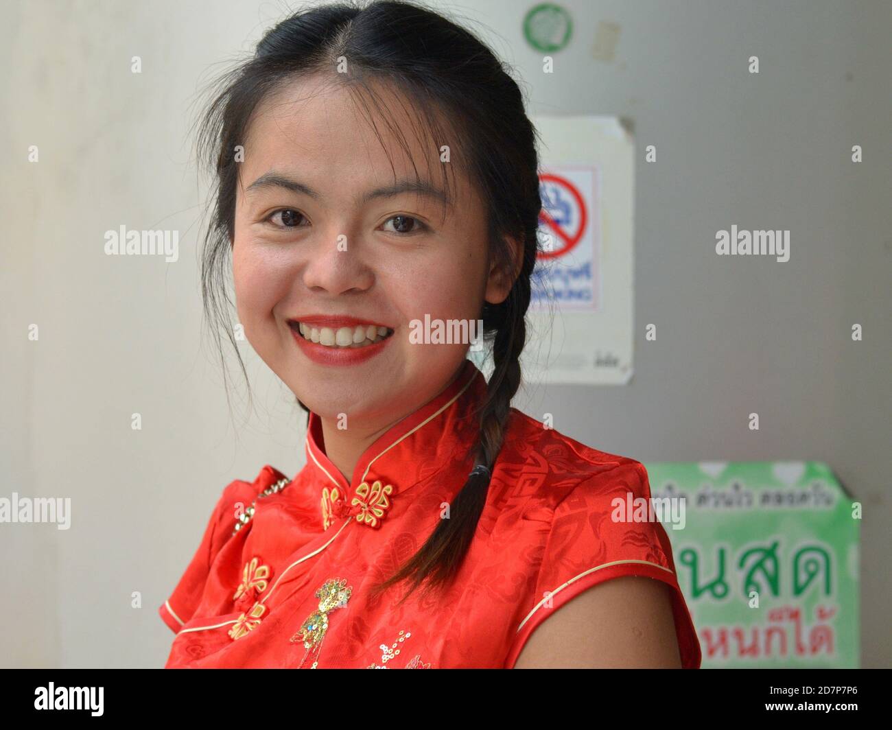 Beautiful young Thai woman with braids wears a red-and-gold traditional Chinese dress (cheongsam) and smiles for the camera during Chinese New Year. Stock Photo
