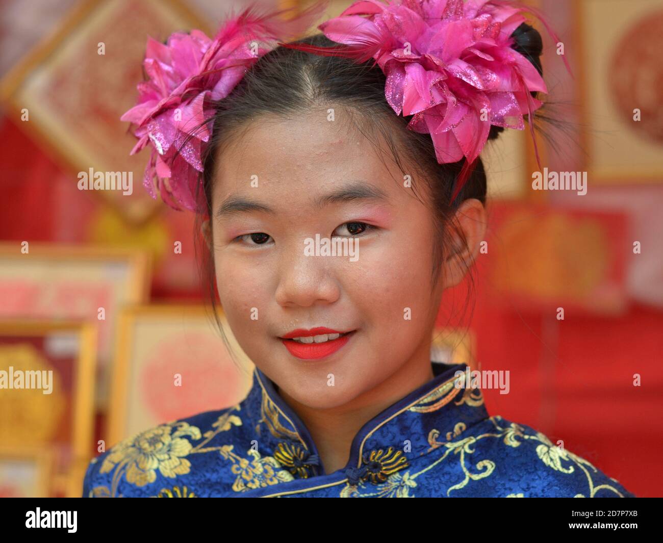 Pretty Thai Chinese pre-teen girl with two traditional Chinese side buns and pink hair ribbons/flowers smiles for the camera during Chinese New Year. Stock Photo