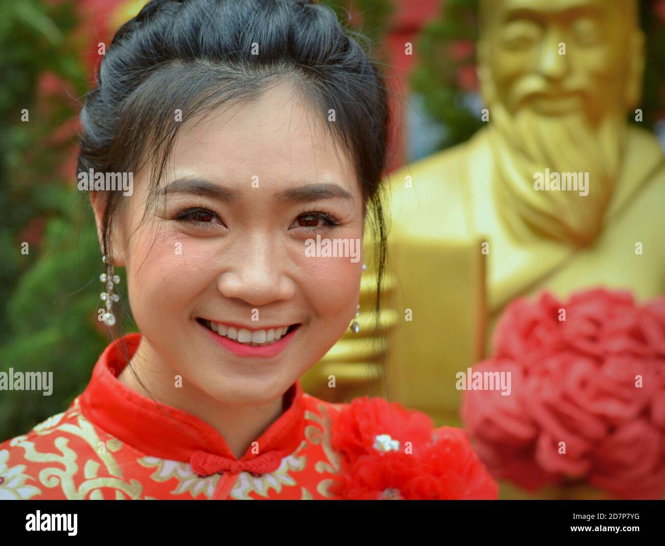 Beautiful young Thai woman wears a red-and-gold traditional Chinese dress (cheongsam) and smiles for the camera during Chinese New Year. Stock Photo