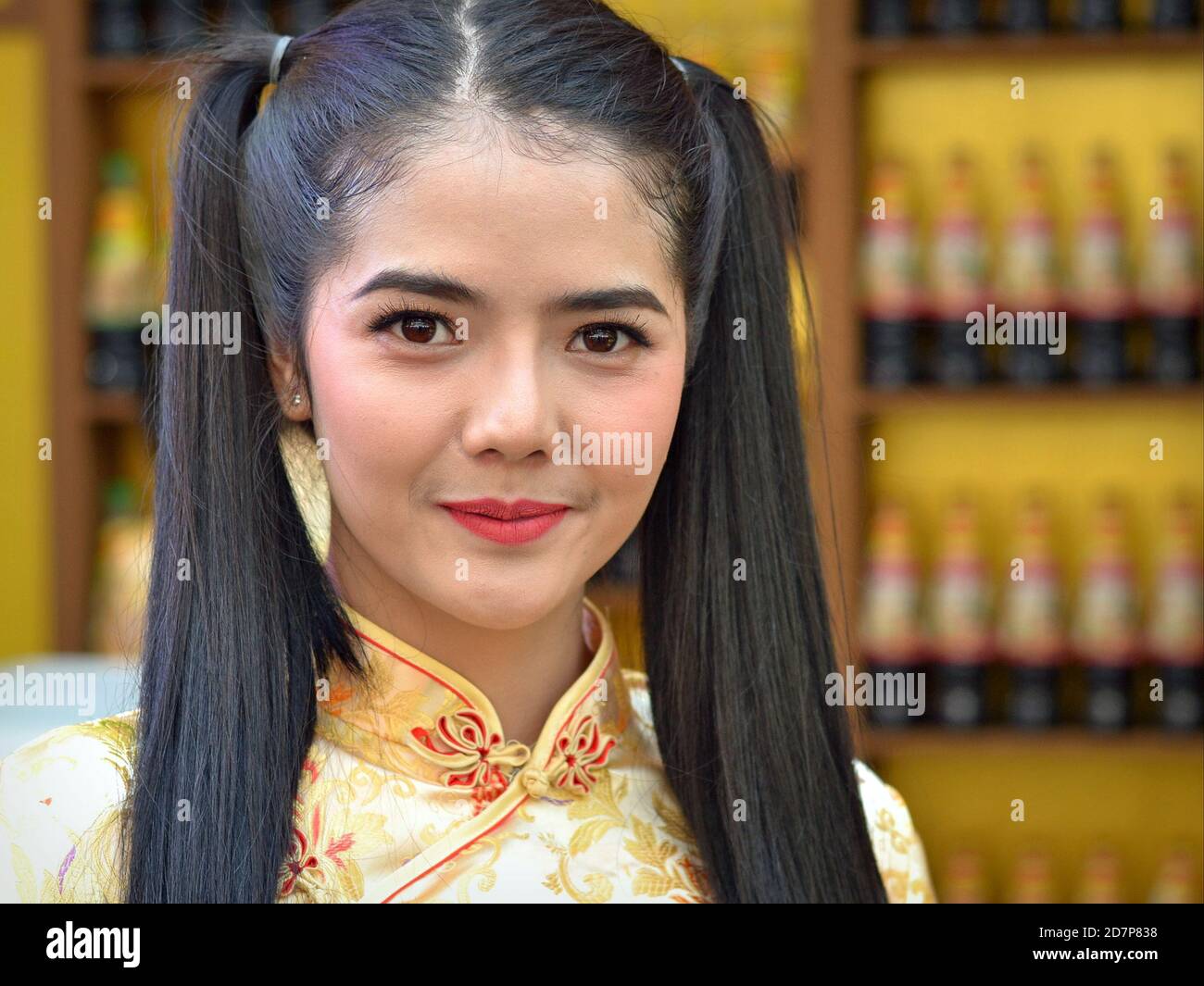 Young Thai beauty with long pigtails wears a yellow traditional silk dress and poses for the camera in Bangkok’s Chinatown during Chinese New Year. Stock Photo