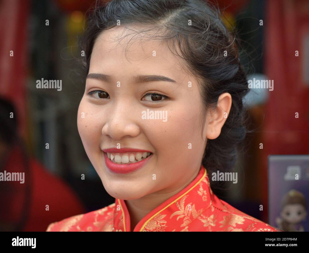 Young Thai Chinese woman wears a traditional red and gold Chinese silk dress and smiles for the camera during Chinese New Year. Stock Photo
