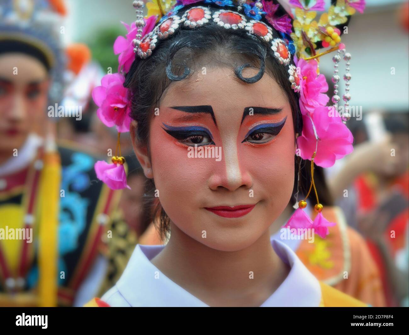 Costumed female Thai Chinese performer with painted traditional Peking opera face mask poses for camera at colorful Chinese New Year street parade. Stock Photo