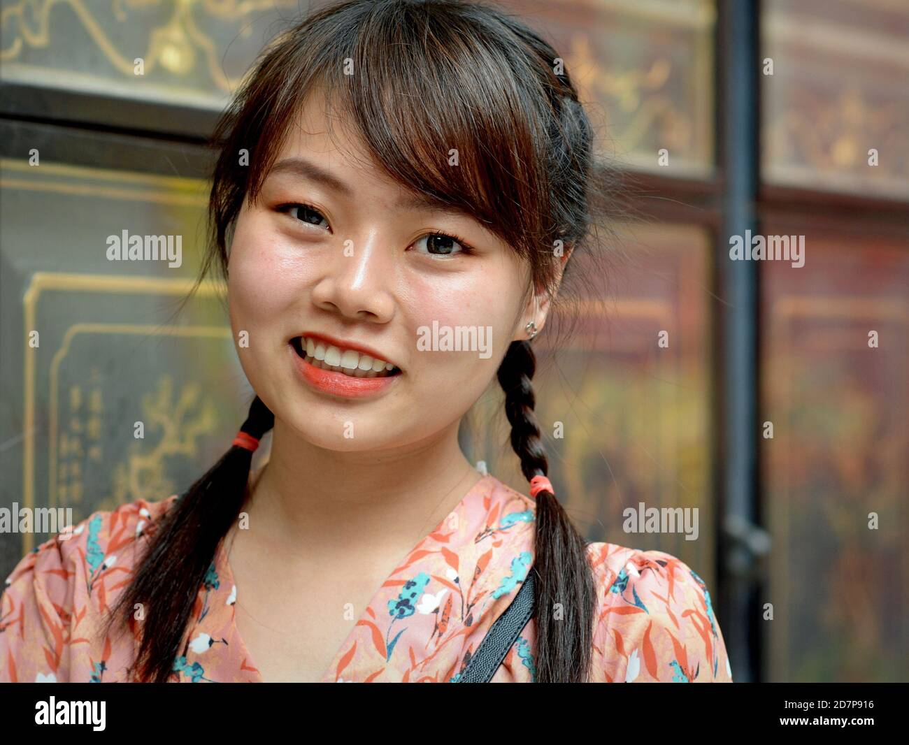 Young Thai Chinese woman with two braids smiles for the camera in Bangkok’s Dragon Lotus Temple (Wat Mangkon Kamala Wat) during Chinese New Year. Stock Photo