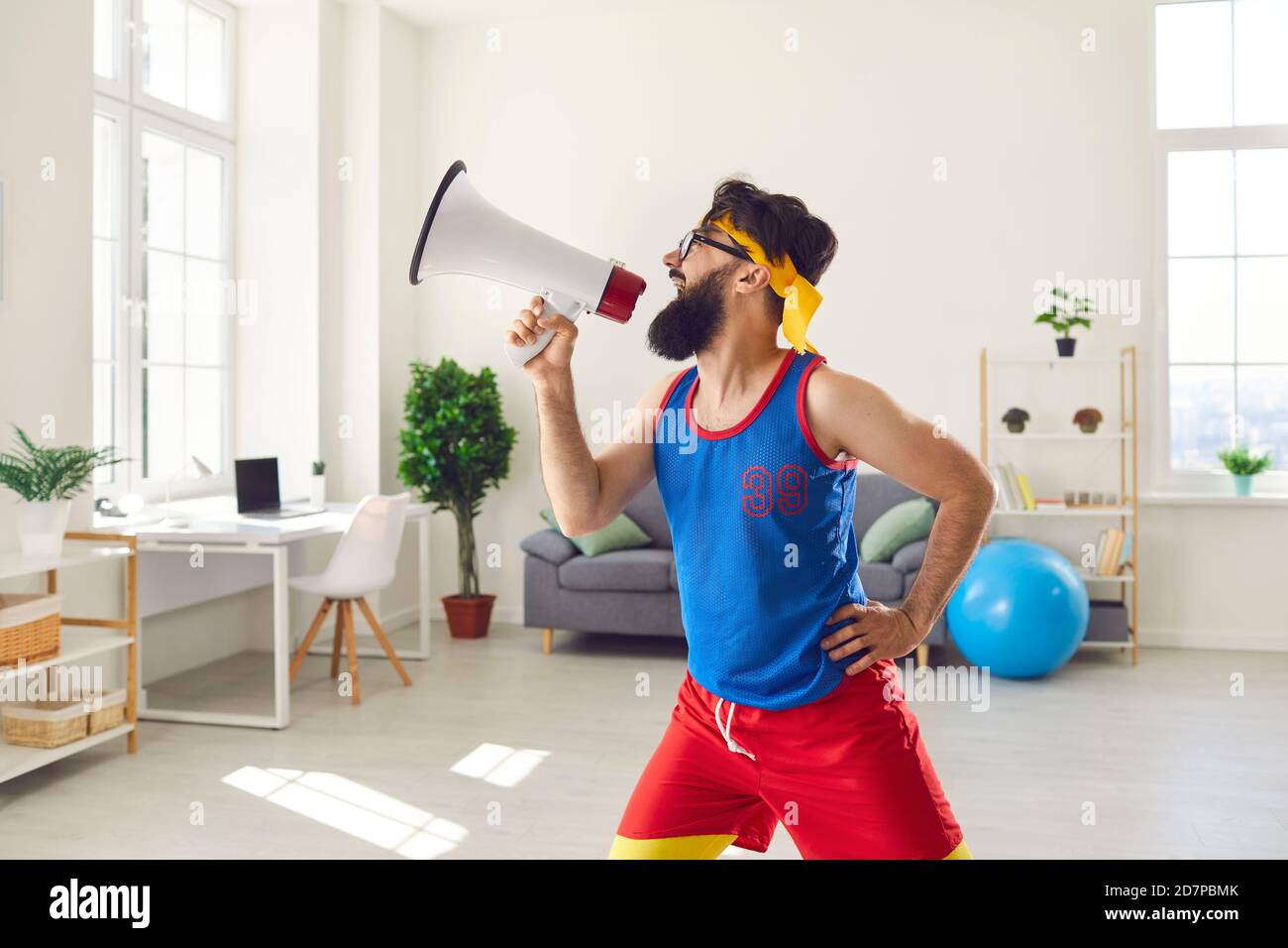 Side view of a funny crazy millennial athlete shouting into a loudspeaker urging everyone to train. Stock Photo